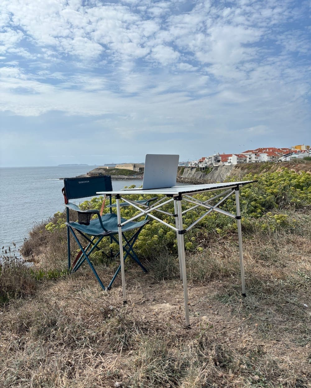 Klapptisch mit Laptop und Campingstuhl auf einer Klippe über dem Meer